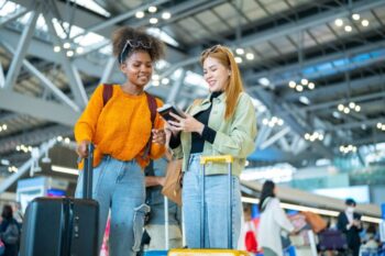 Two woman friends with luggage walking together at Airport terminal.